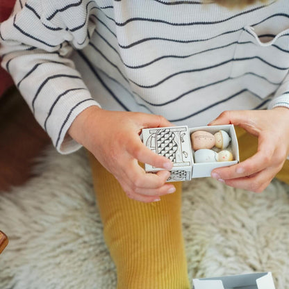 A child opens a small box with a bed on it's front to reveal two sleeping figurines from the Grapat 2026 Advent Calendar.