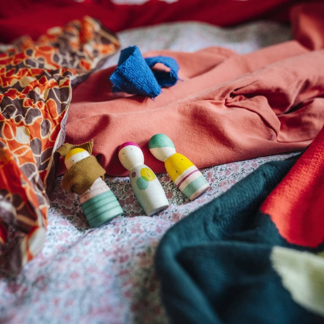 3 wooden figures from the Grapat 2026 Advent Calendar laying on colorful scraps of cloth.