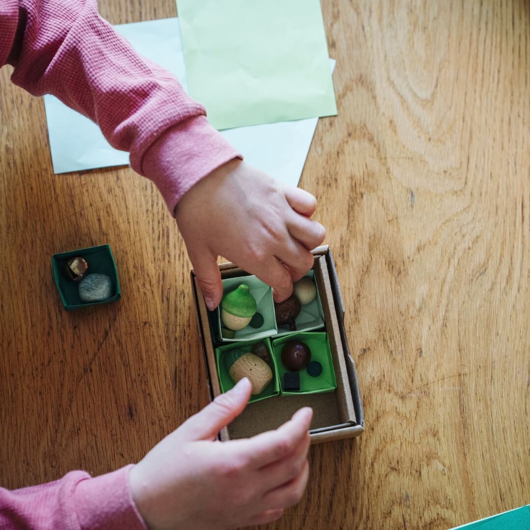 A child reaches into a small box filled with found treasures and pieces from the Grapat 2026 Advent Calendar.