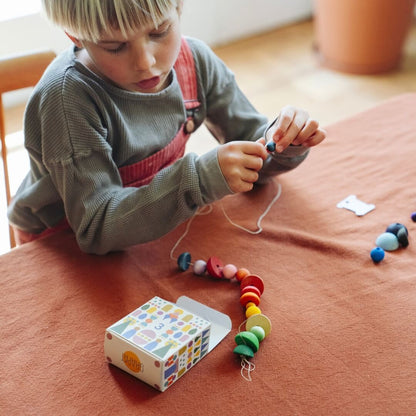 A child strings colorful rainbow beads from the Grapat 2026 Advent Calendar to make a rainbow garland.